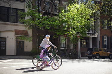 Side view of mother and daughter riding bicycles on street - CAVF15951