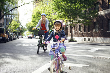 Portrait of happy mother and daughter riding bicycles on street - CAVF15957