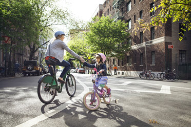 Mutter und Tochter geben sich beim Fahrradfahren auf der Straße die Hand - CAVF15958