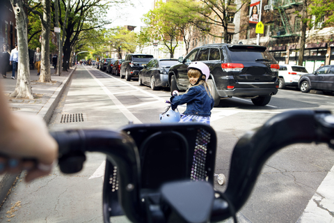 Mädchen schaut Mutter an, während sie auf der Straße Fahrrad fährt, lizenzfreies Stockfoto