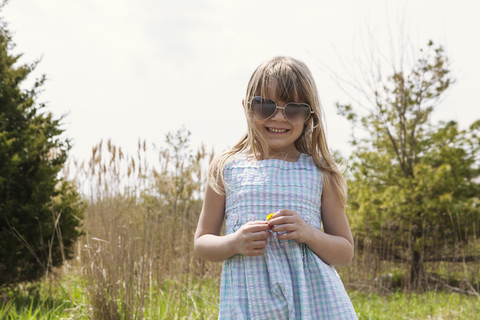 Porträt eines glücklichen Mädchens, das auf einem Feld vor dem Himmel steht, lizenzfreies Stockfoto