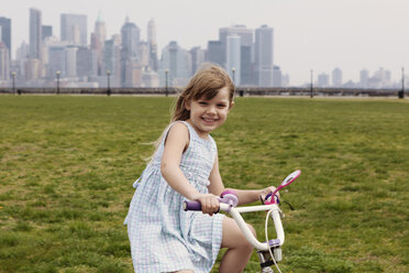 Porträt eines glücklichen Mädchens beim Fahrradfahren mit Skyline im Hintergrund - CAVF15975