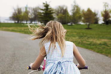Seitenansicht eines Fahrrad fahrenden Mädchens auf einer Straße neben einem Feld - CAVF15981
