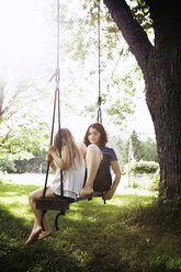 Sisters sitting on swing at grass field - CAVF15997