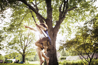 Low angle view of sisters enjoying at swing in park - CAVF15999