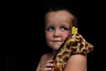 Thoughtful shirtless boy looking away while holding toy against black background - CAVF16020