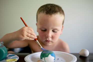 Hemdloser Junge, der Ostereier färbt, während er zu Hause am Tisch sitzt - CAVF16027