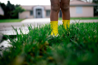 Low section of boy standing on wet grassy field during rainy season - CAVF16029