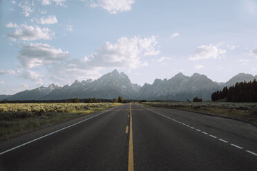 Empty country road amidst field leading towards mountains against sky - CAVF16041