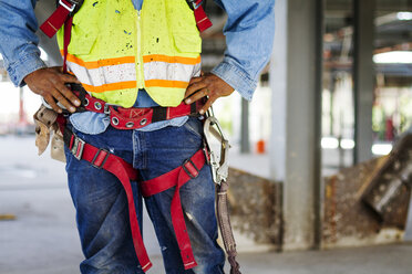 Midsection of manual worker wearing safety harness standing at construction site - CAVF16057