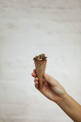 Cropped image of man holding ice cream cone against wall - CAVF16122