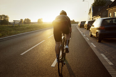 Rear view of man cycling on road by parked cars against sky - CAVF16124