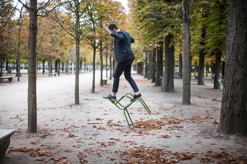 Full length of businessman playing on chair at park - CAVF16137