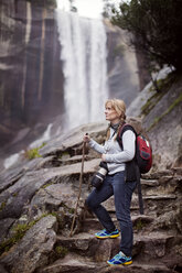 Nachdenkliche Frau beim Wandern gegen einen Wasserfall im Wald - CAVF16146