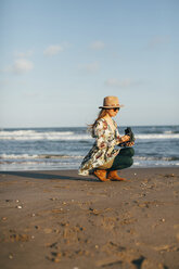 Frau hält Kamera kauernd am Strand gegen den Himmel an einem sonnigen Tag - CAVF16153