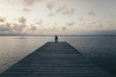 Rückansicht einer Frau, die bei Sonnenuntergang auf einem Steg über dem Meer sitzt - CAVF16162