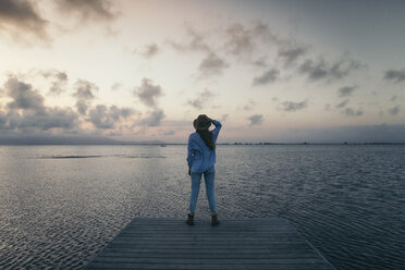 Rear view of woman standing on pier over sea against sky during sunset - CAVF16163