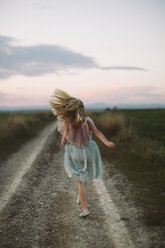 Rear view of girl running on dirt road during sunset - CAVF16166