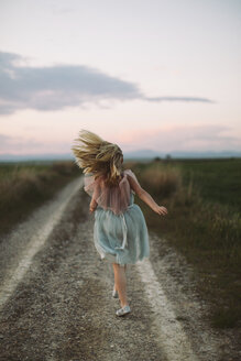 Rückansicht eines Mädchens, das bei Sonnenuntergang auf einem Feldweg läuft - CAVF16166