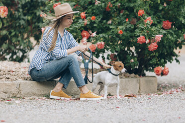 Frau streichelt Jack Russell Terrier, während sie bei Pflanzen sitzt - CAVF16170