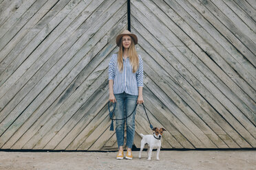 Porträt einer Frau mit Jack Russell Terrier, die vor einem Holztor steht - CAVF16171