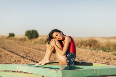 Woman hugging knees while sitting at field against clear sky - CAVF16177