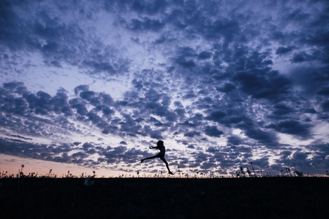 Silhouette Mädchen springt auf Feld gegen dramatischen Himmel, lizenzfreies Stockfoto