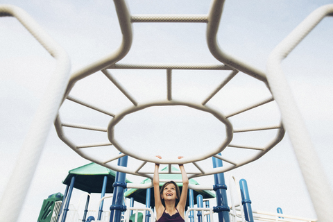 Verspieltes Mädchen hängt am Klettergerüst auf dem Spielplatz, lizenzfreies Stockfoto