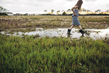 Side view of messy girl walking on wet field - CAVF16214