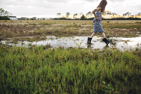 Seitenansicht eines unordentlichen Mädchens, das auf einem nassen Feld läuft - CAVF16214