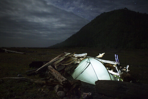 Beleuchtetes Zelt und Baumstämme auf einem Feld gegen den bewölkten Himmel bei Nacht - CAVF16250