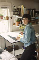 Porträt einer Künstlerin, die einen Stift hält und an einem Tisch steht - CAVF16293