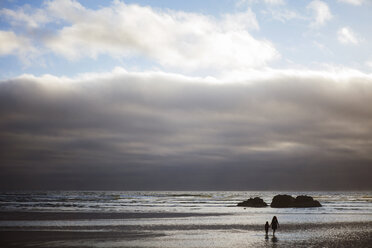 Mother and daughter walking at beach against cloudy sky - CAVF16300