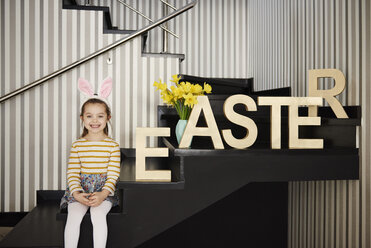 Porträt eines lächelnden Mädchens mit Hasenohren, das auf einer Treppe neben dem Wort 