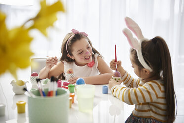 Sisters sitting at table painting Easter eggs - ABIF00167