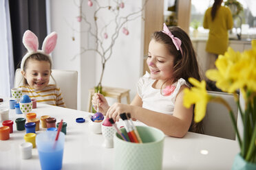 Sisters sitting at table painting Easter eggs - ABIF00172