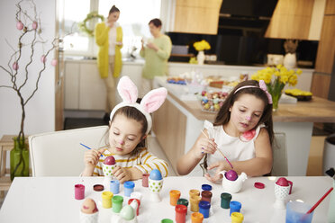 Sisters sitting at table painting Easter eggs - ABIF00173