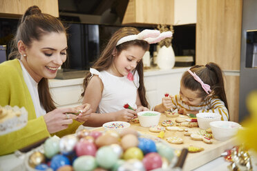 Mutter mit Töchtern beim Verzieren von Osterkeksen in der Küche - ABIF00175
