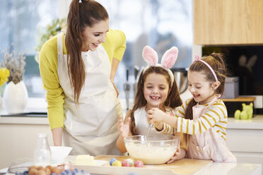 Glückliche Mutter und Töchter backen gemeinsam Osterkekse in der Küche - ABIF00184