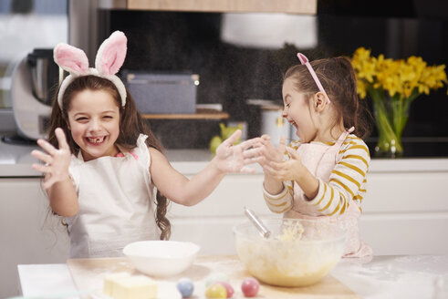 Two playful sisters having fun baking Easter cookies in kitchen together - ABIF00187