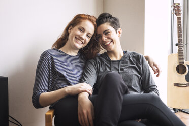 Glückliches lesbisches Paar sitzt auf einem Stuhl zu Hause - CAVF16358
