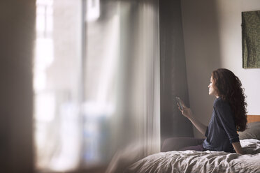 Frau benutzt Mobiltelefon, während sie zu Hause auf dem Bett sitzt - CAVF16389