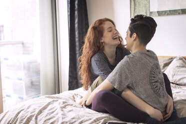 Cheerful lesbians sitting face to face on bed at home - CAVF16392