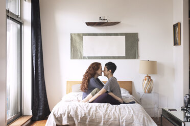 Seitenansicht von romantischen Lesben, die sich auf dem Bett sitzend die Nasen reiben - CAVF16393