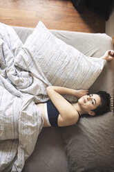 Hochformatiges Porträt einer Frau, die zu Hause auf dem Bett liegt - CAVF16396