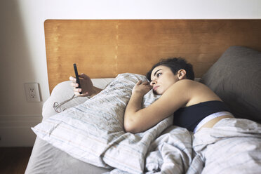 Frau benutzt Mobiltelefon beim Entspannen auf dem Bett - CAVF16397