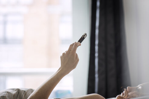 Frau benutzt Smartphone, während sie zu Hause auf dem Bett liegt - CAVF16405