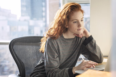 Confident woman using laptop computer while sitting by window - CAVF16428