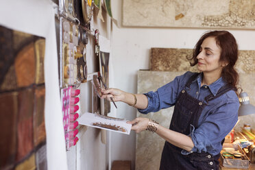 Artist putting artwork on wall in workshop - CAVF16457