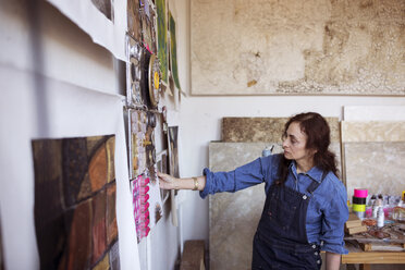 Artist looking paintings on wall in workshop - CAVF16465